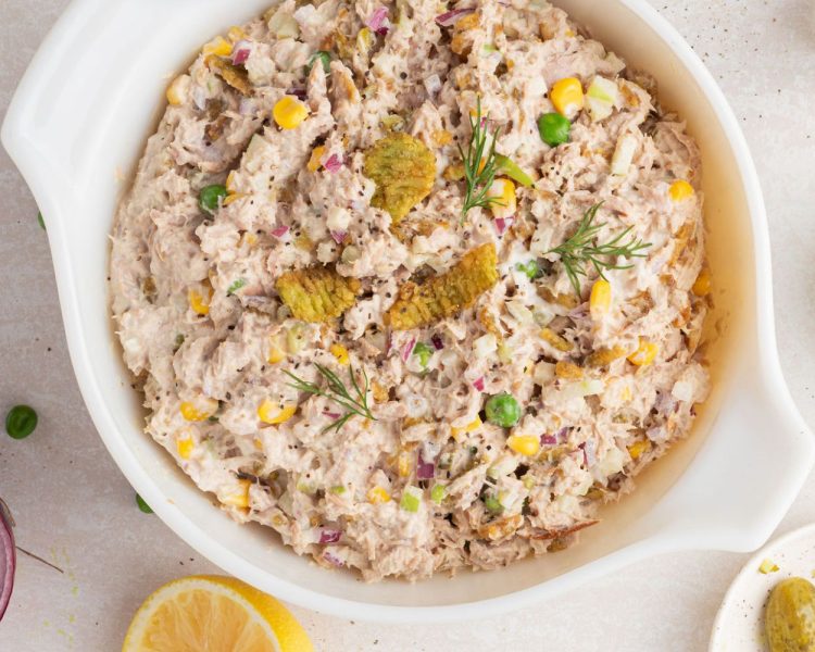 White bowl with tuna salad including corn, crispy jalapeno, peas, pickles, and red onion, topped with sprigs of dill.