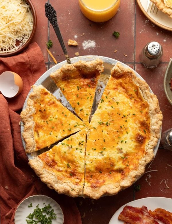 Whole baked quiche topped with green onion in a silver pie pan with small pieces missing.