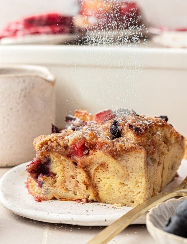 Powdered sugar being sprinkled over a slice of French Toast casserole with berries.