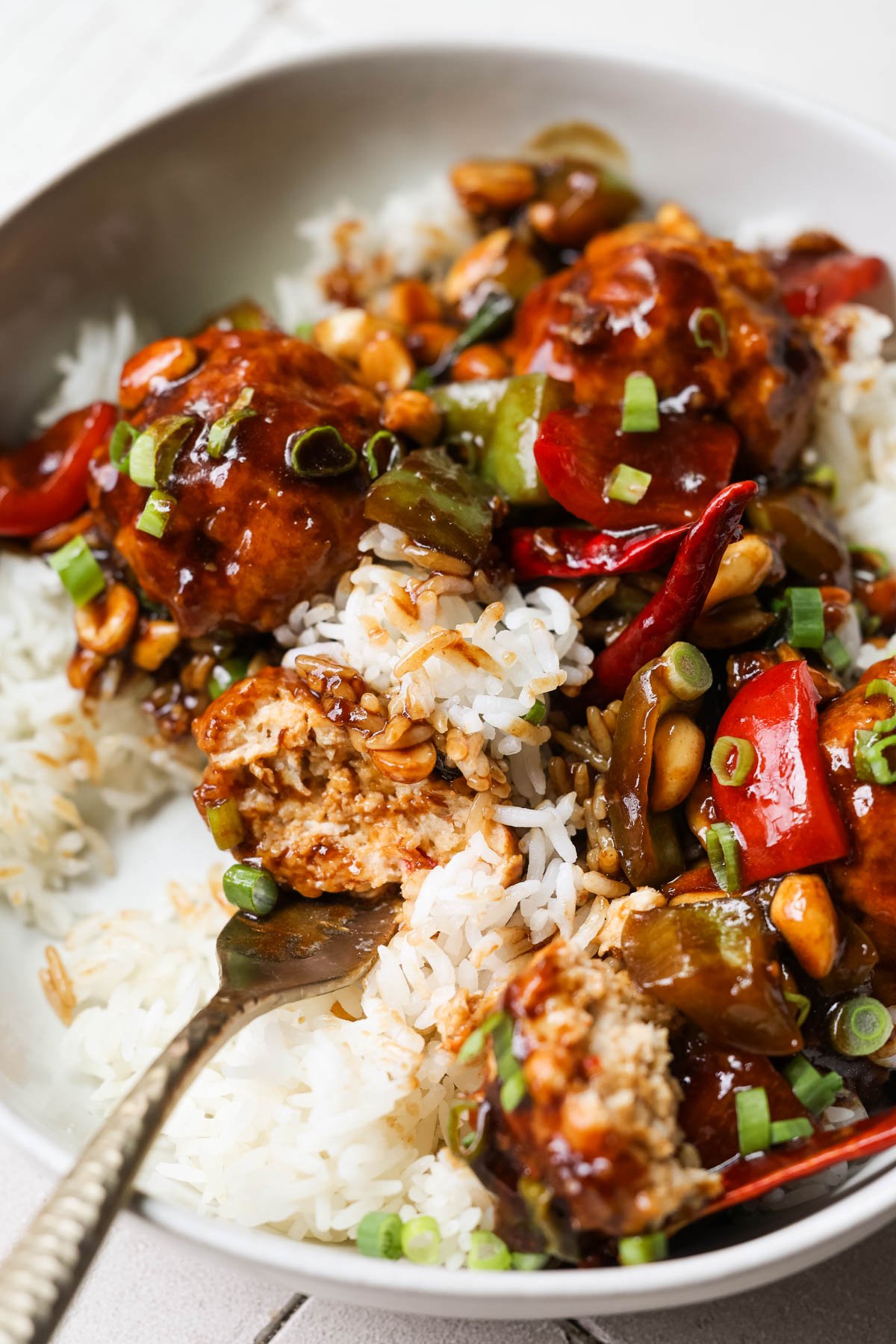 a fork taking a bite of chicken meatballs in a kung pao sauce with white rice. 