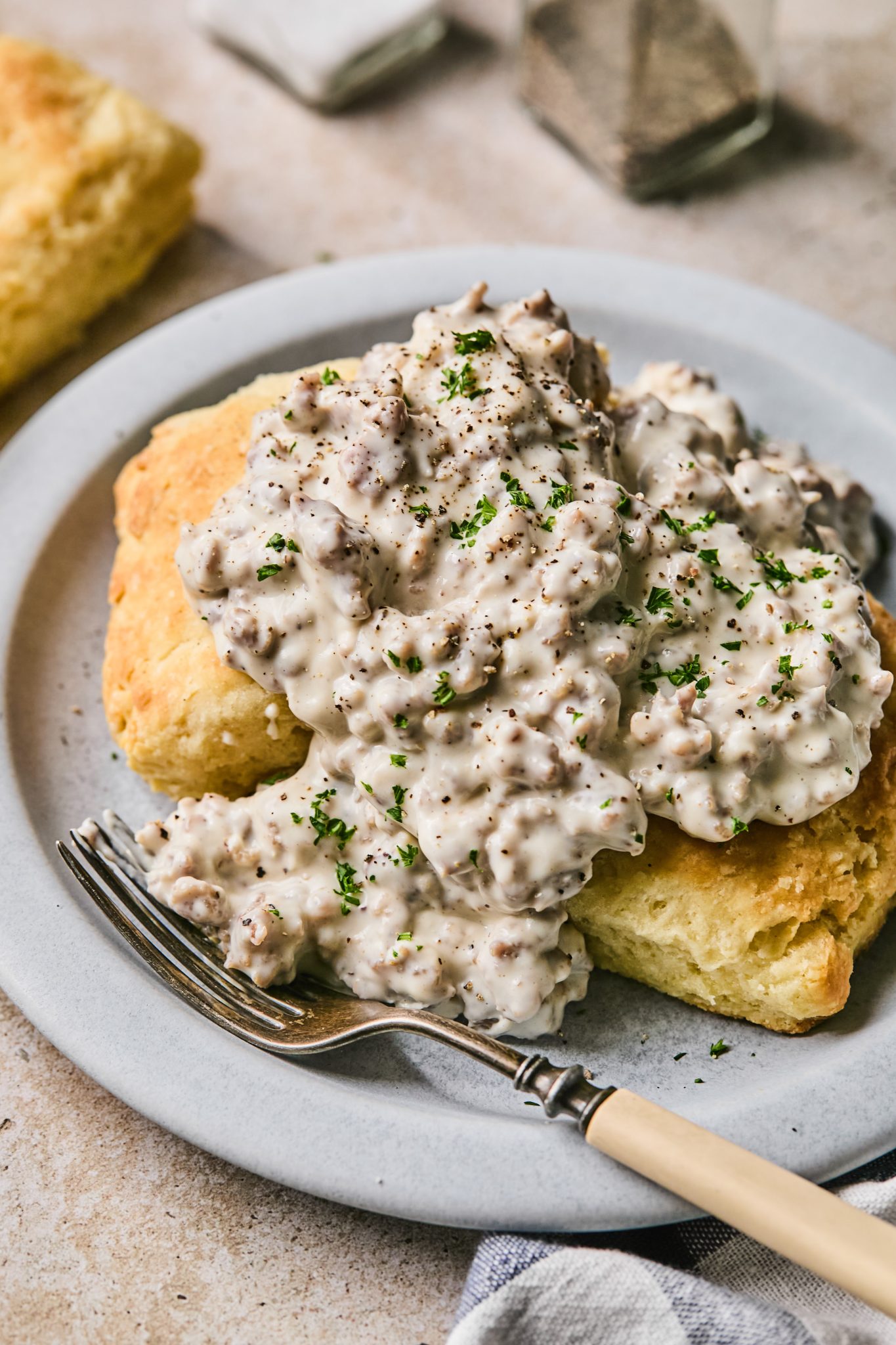 biscuits and sausage gravy on a plate garnished with fresh parsley on top. 