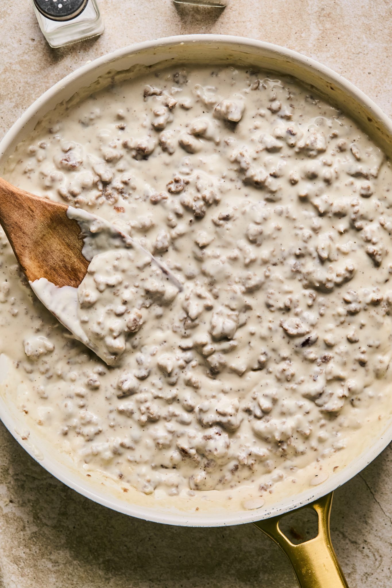 a frying pan with sausage gravy in it with a wooden spoon. 