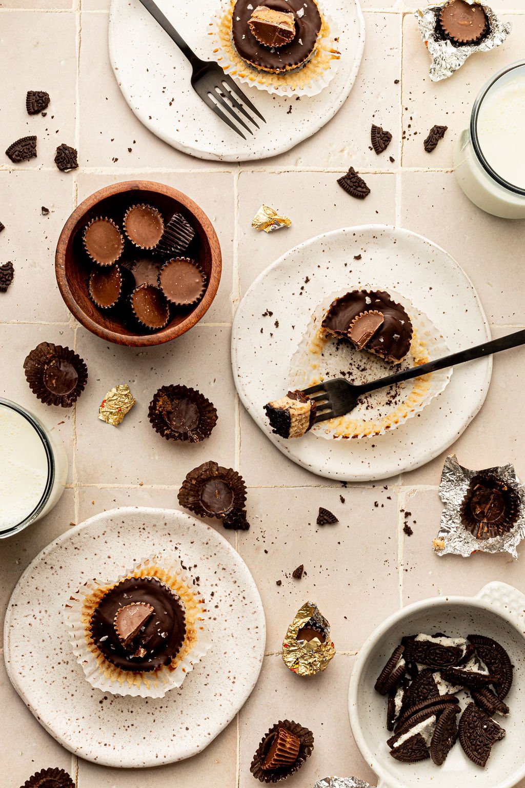 Plates with peanut butter cheesecake bites. Surrounded by peanut butter cups, chocolate chips, and crushed oreos.