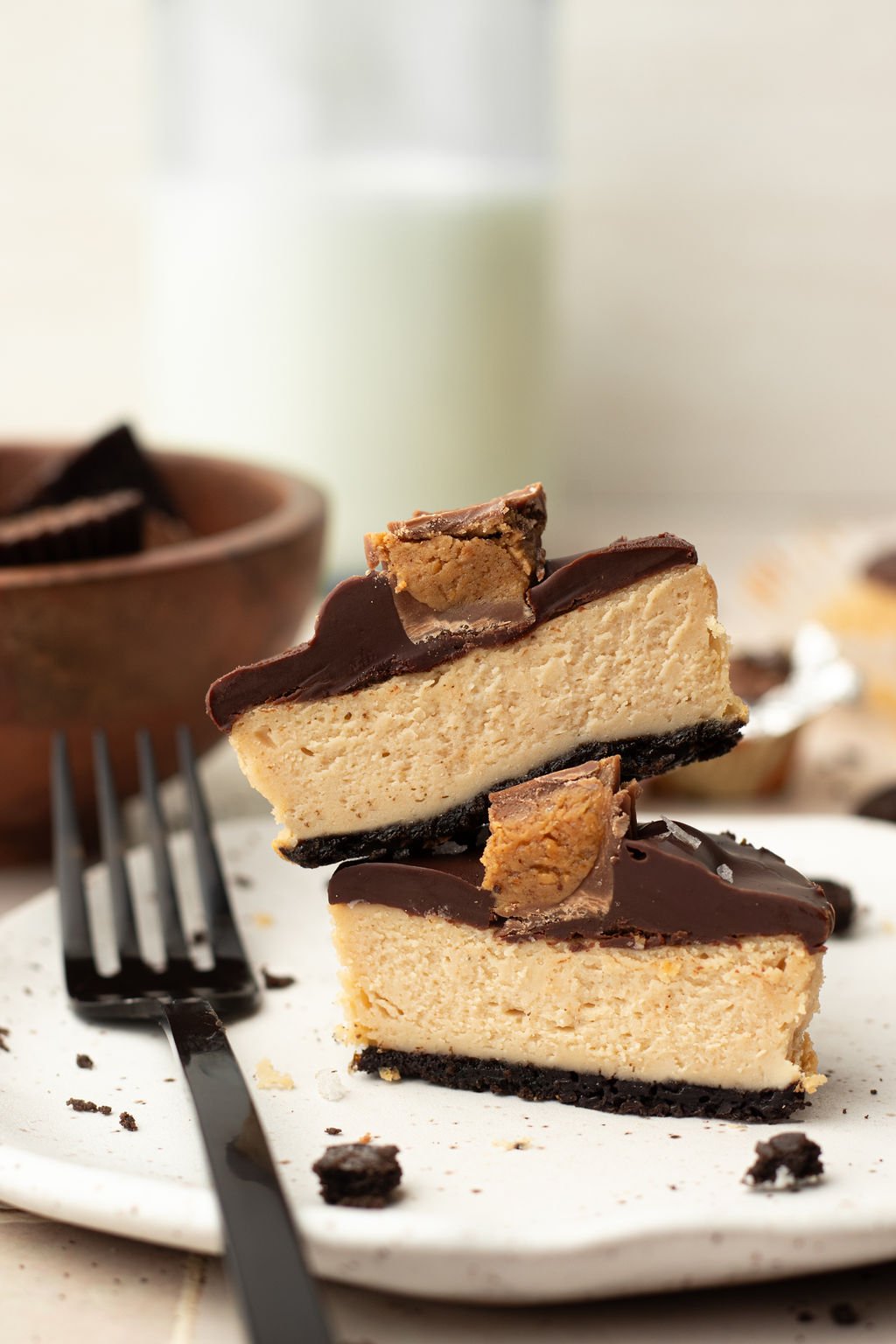 Circular cheesecake cut in half and stacked on one another. Topped with a layer of chocolate and half of a mini reeses.