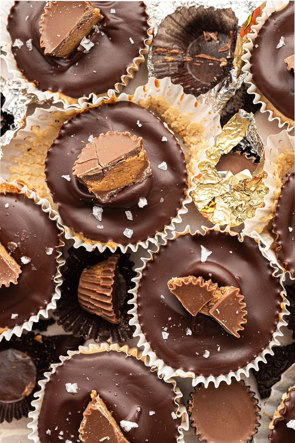 Multiple mini cheesecake bites with chocolate ganache topping, half of a reeses cup, and flaky sea salt