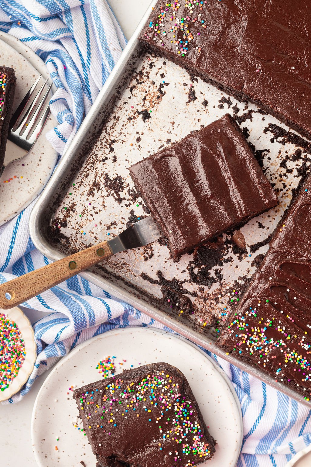 Offset spatula removing a piece of chocolate cake with chocolate frosting off of a silver half sheet pan.