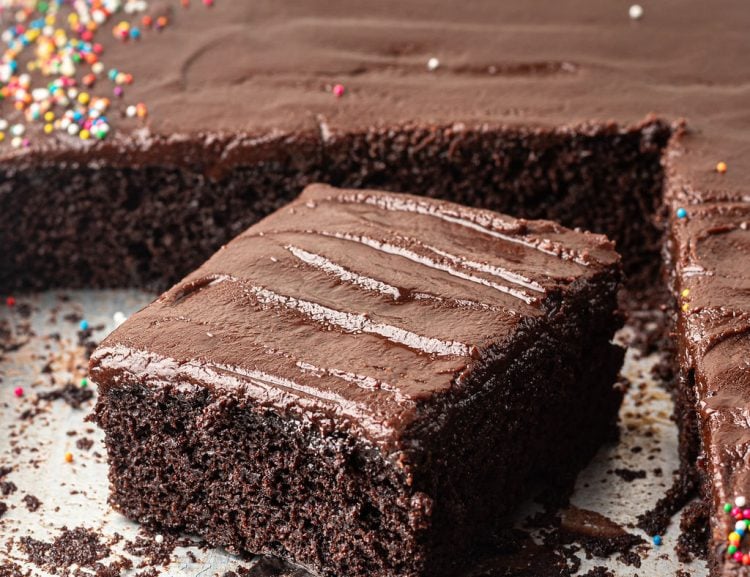 Chocolate sheet cake with multi colored sprinkles on a half sheet pan with one slice removed with an offset spatula.