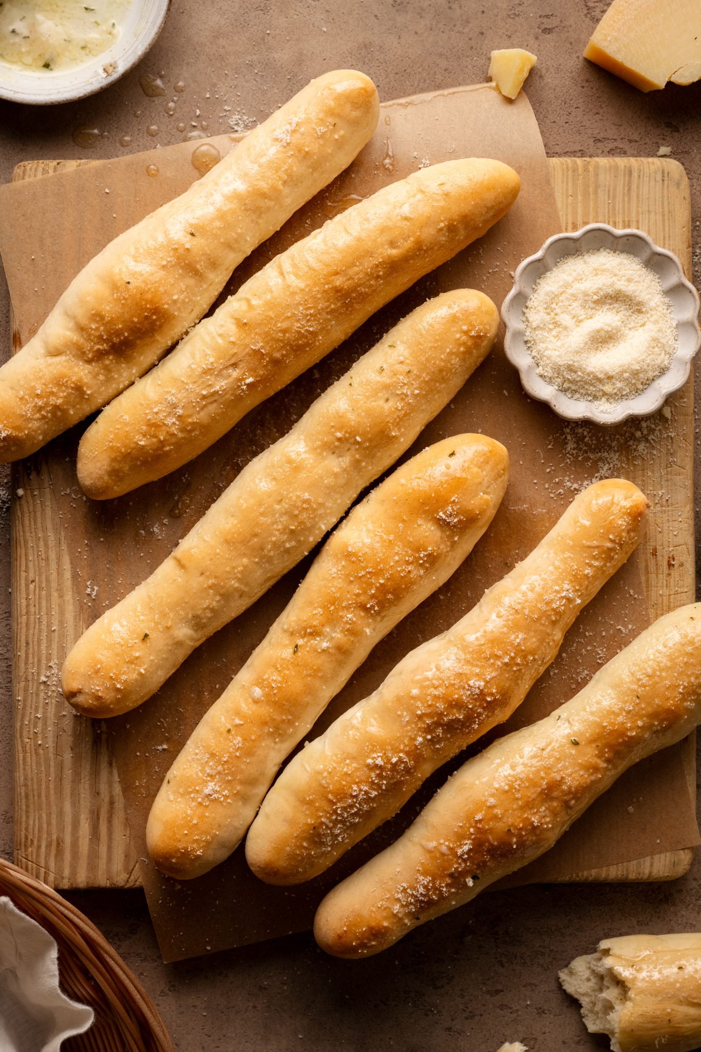 copycat olive garden breadticks recipe on a wooden cutting board lined with parchment paper and butter spread on top of the bread. 