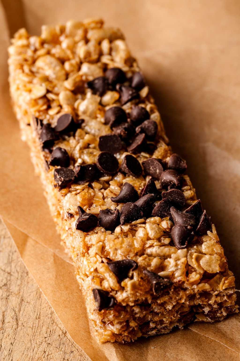 a close up image of a granola bar on parchment paper with mini chocolate chips on top. 