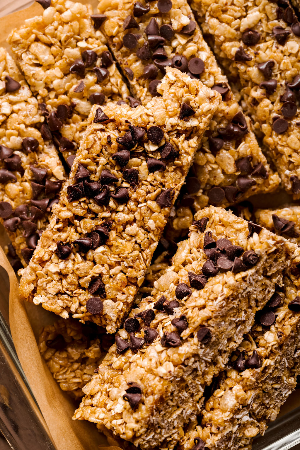 a close up image of granola bars with a bite taken out of one of them on parchment paper with mini chocolate chips on top. 