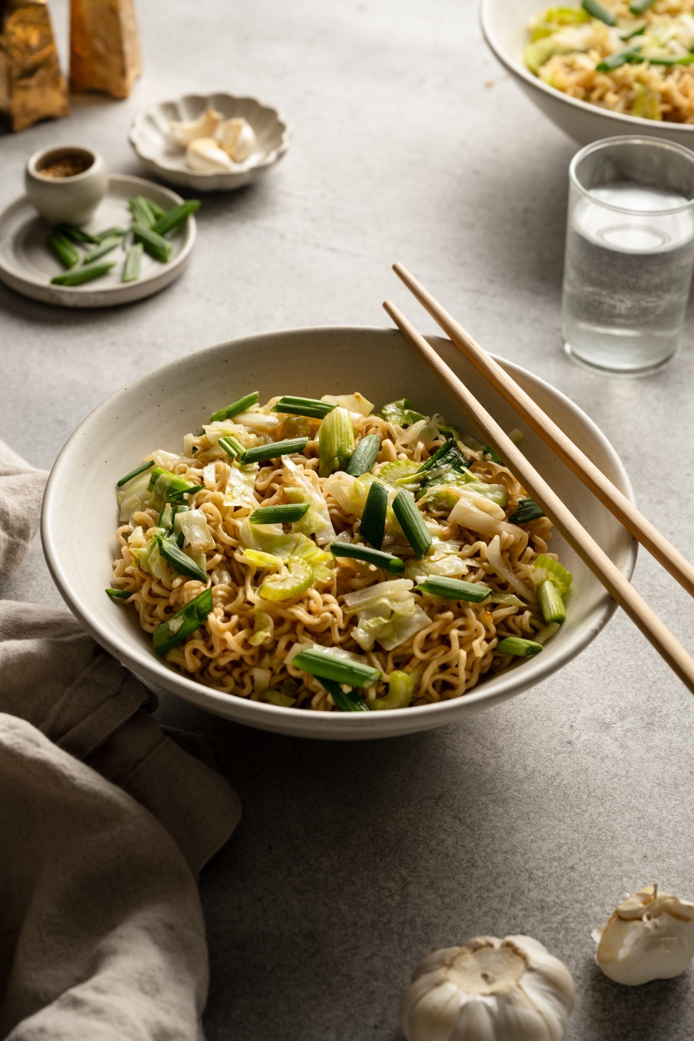 a bowl of chow bein with green onion on top and chopsticks on the side of the bowl. 