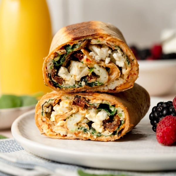 A whole wheat tortilla filled with an egg white, spinach, sun dried tomato, and feta mixture. Cut into two pieces stacked on one another.