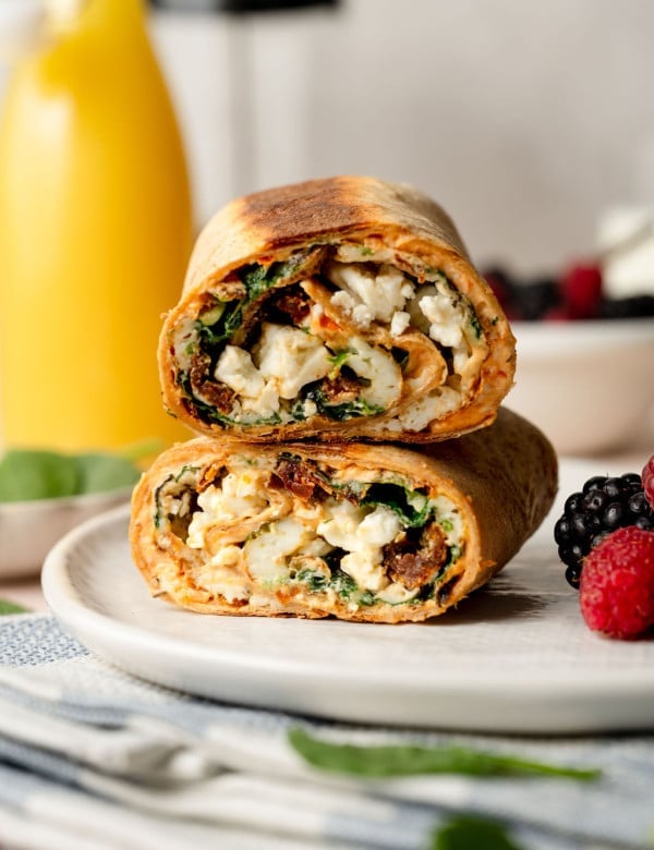 A whole wheat tortilla filled with an egg white, spinach, sun dried tomato, and feta mixture. Cut into two pieces stacked on one another.