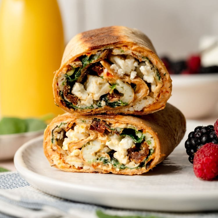 A whole wheat tortilla filled with an egg white, spinach, sun dried tomato, and feta mixture. Cut into two pieces stacked on one another.