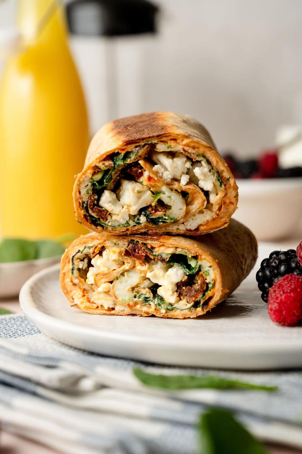 A whole wheat tortilla filled with an egg white, spinach, sun dried tomato, and feta mixture. Cut into two pieces stacked on one another.