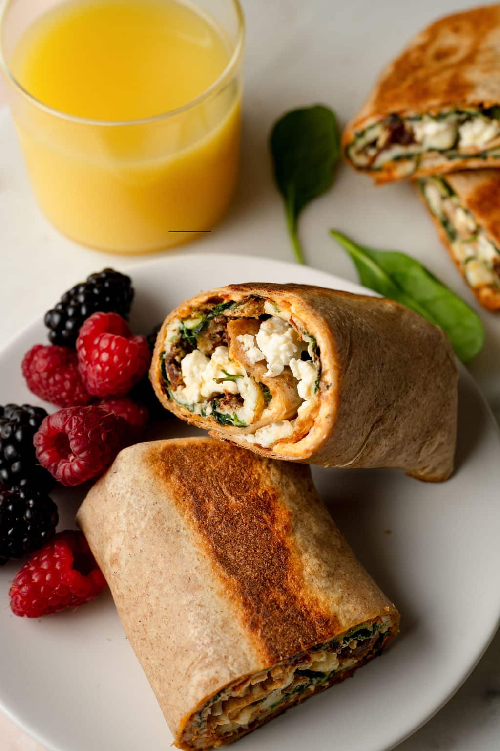 Overhead shot of a spinach, feta, egg white wrap in a whole wheat tortilla, on a white plate with raspberries and blackberries.