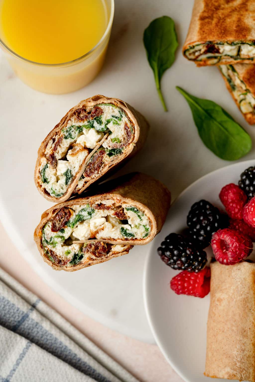 Overhead shot of inside of an egg white spinach wrap with sun dried tomatoes and feta, next to a plate with blackberries and raspberries.