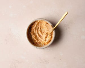 A white bowl with a creamy sun-dried tomato spread with a gold spoon in it.