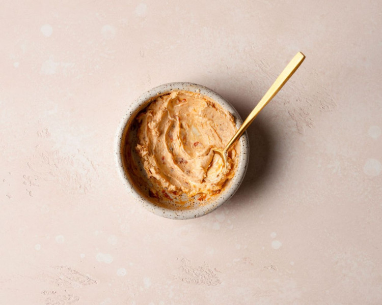 A white bowl with a creamy sun-dried tomato spread with a gold spoon in it.