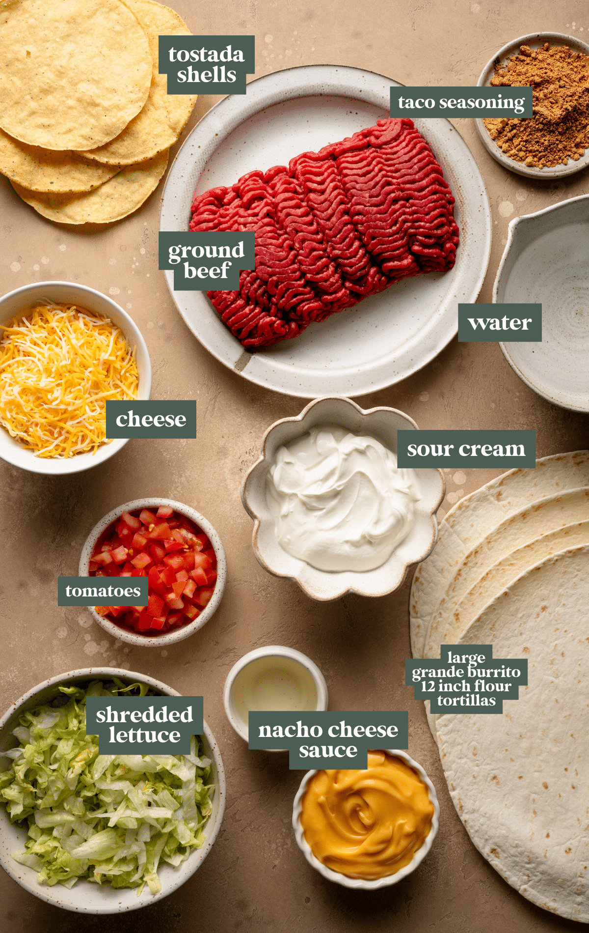 Flat lay of Crunchwrap Supreme ingredients arranged on a neutral-toned surface. Labeled components include tostada shells, ground beef, taco seasoning, water, shredded cheese, sour cream, diced tomatoes, shredded lettuce, nacho cheese sauce, and large 12-inch flour tortillas. Each ingredient is placed in bowls or on plates, showcasing the fresh and vibrant elements needed to make a homemade Crunchwrap Supreme.