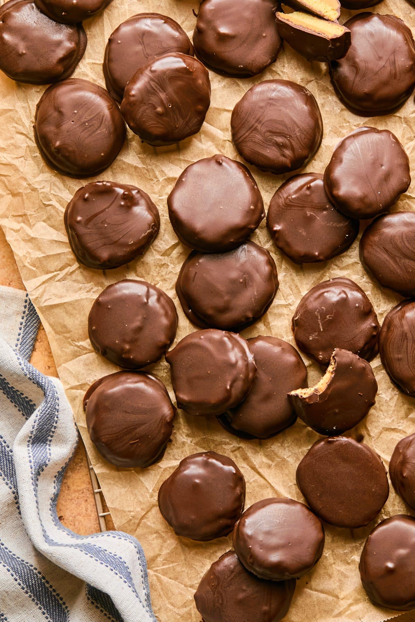 A batch of round, chocolate-coated copycat Tagalong cookies arranged on crinkled parchment paper, with one cookie partially bitten to reveal its golden peanut butter filling.






