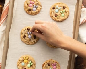 A person is pressing pastel M&M candies into freshly baked cookies to create a bunny design.