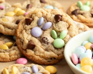 Close-up of soft and chewy cookies with pastel M&Ms in the shape of bunnies and chocolate chips, arranged on a wooden surface with extra candies around.