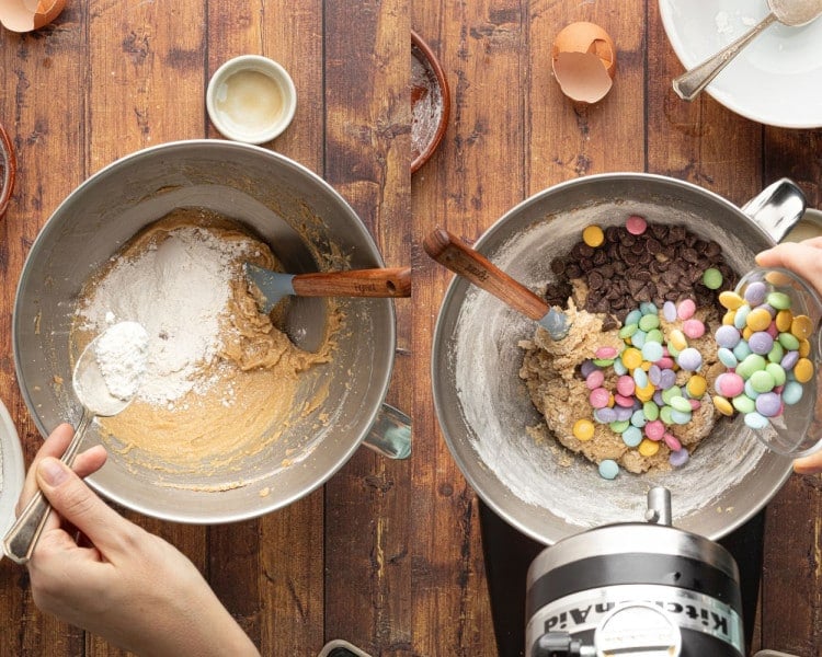 A side-by-side image showing two stages of mixing cookie dough. On the left, a person is adding dry ingredients, including flour and baking powder, to the wet mixture in a mixing bowl with a spatula. On the right, pastel-colored M&Ms and chocolate chips are being poured into the fully mixed dough. The bowls sit on a rustic wooden surface with eggshells and measuring spoons scattered around.