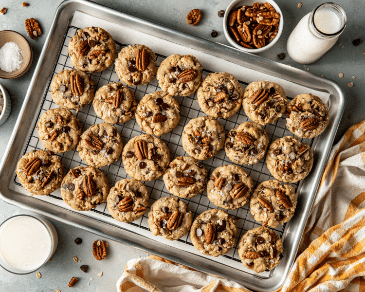 Tray of baked cowboy cookies on top of wire cooling rack on metal sheet pan lined with parchment paper.