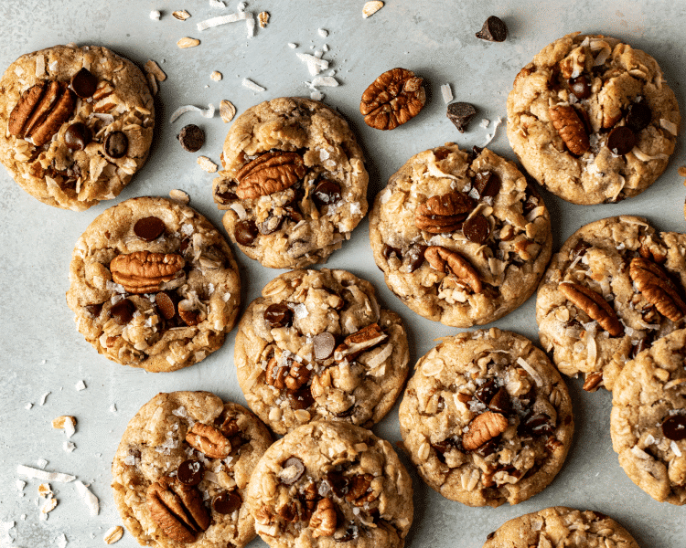 Cowboy cookies topped with chocolate chips, pecans and shredded coconut on table.