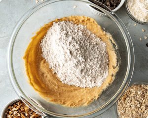 Adding the dry ingredients to the wet ingredients for Cowboy cookies in glass mixing bowl.