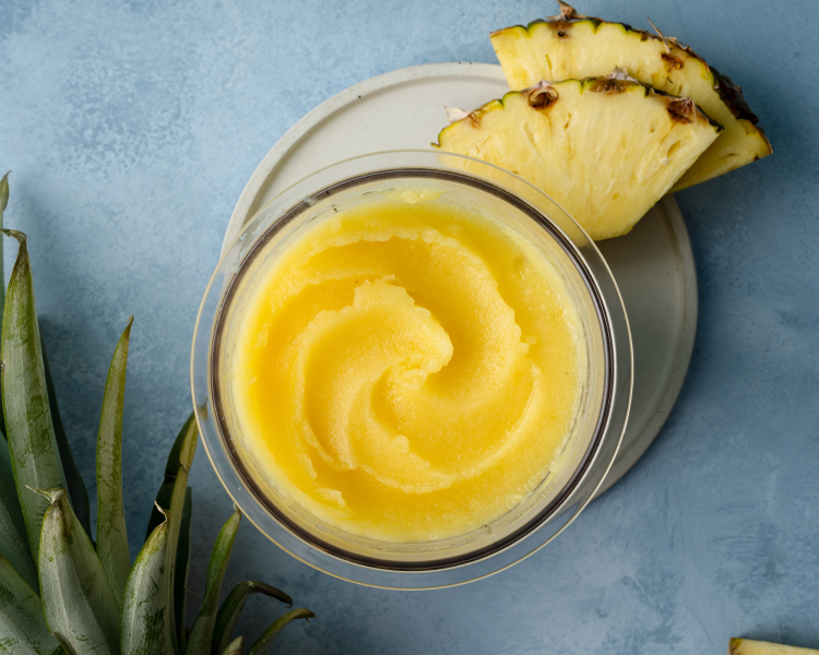 Nina creami Pineapple sorbet in pint container on white plate with two pineapple chunks garnishing the plate.