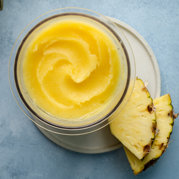 Pineapple sorbet in ninja creami pint container on white plate with two pineapple chunks garnishing the plate.