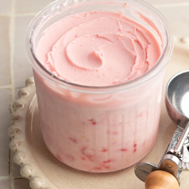 Ninja creami strawberry frozen yogurt in pint container after spinning on cream plate with ice cream scoop beside it.