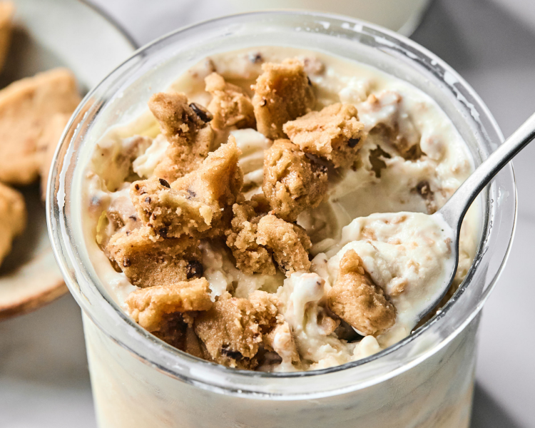Vanilla protein ice cream topped with cookie dough with spoon digging up the top.