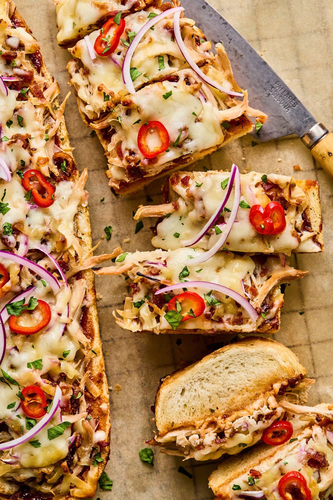 Overhead shot of several BBQ chicken French bread pizza slices topped with cheese, red onion, and fresh herbs on a parchment-lined wire rack.