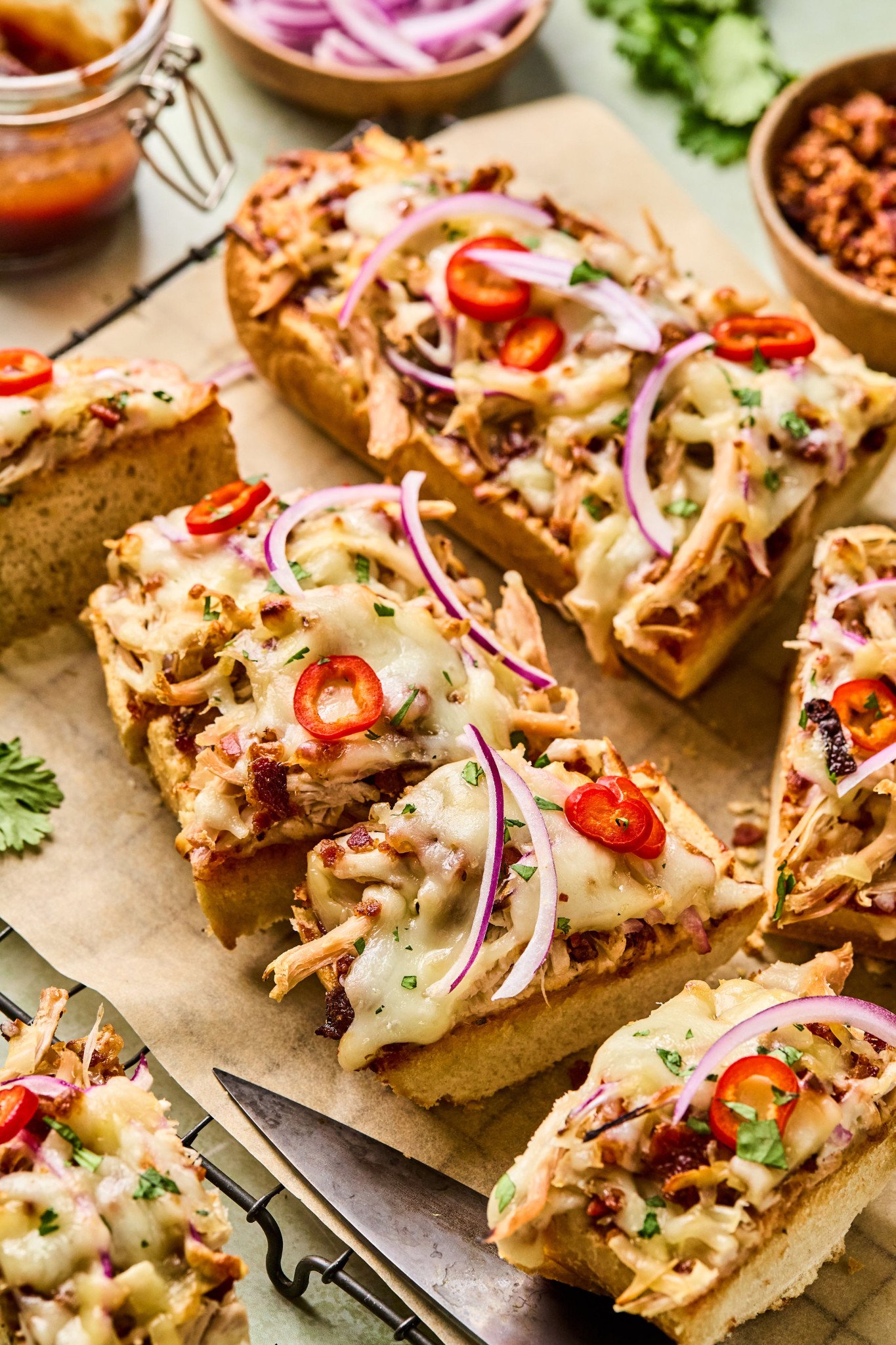 Close-up of a slice of BBQ chicken French bread pizza topped with melted cheese, barbecue sauce drizzle, red onion, and sliced red chili peppers.