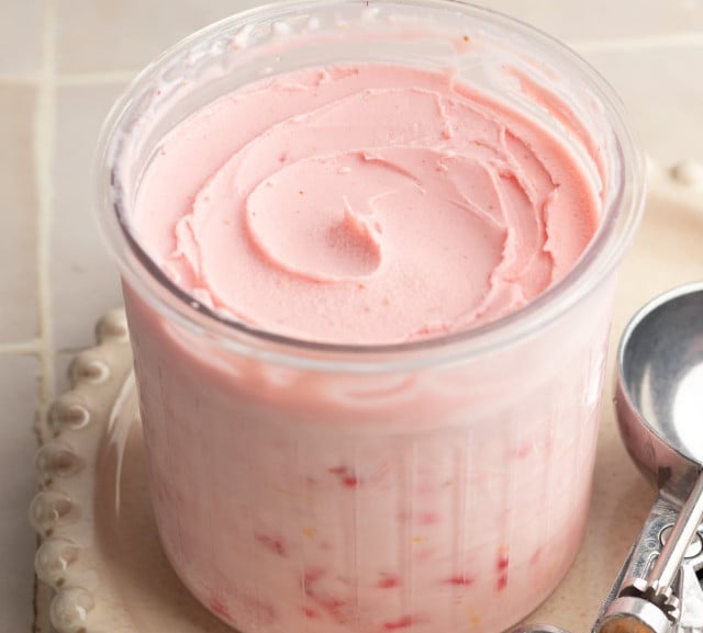 Ninja creami strawberry frozen yogurt in pint container after spinning on cream plate with ice cream scoop beside it.