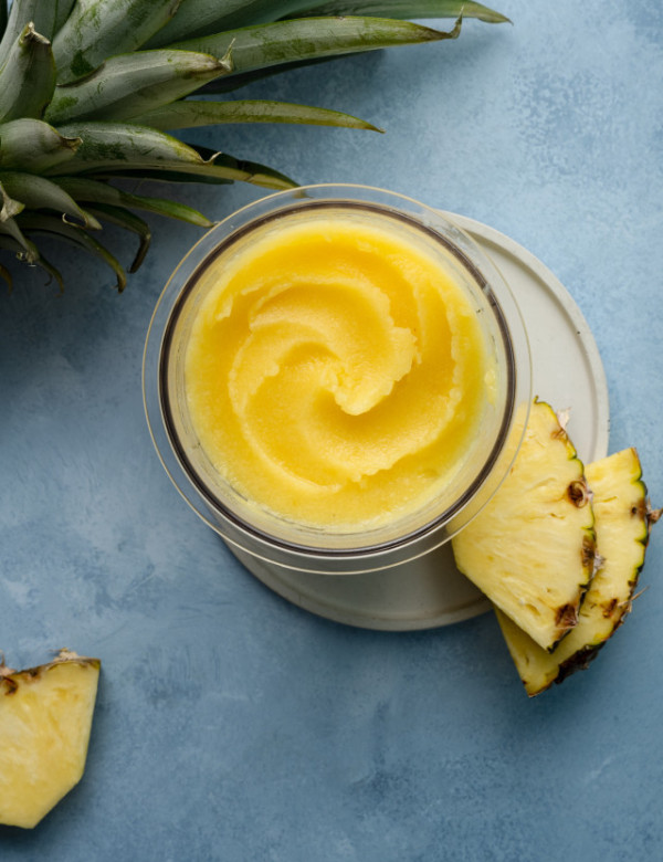 Ninja creami pineapple sorbet in pint container on plate garnished with two pineapple chunks.