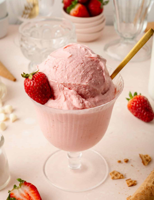 Strawberry ice cream (ninja creami) in glass bowl with gold spoon and fresh strawberry on the side.