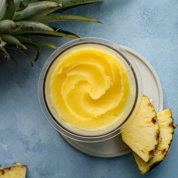 Ninja creami pineapple sorbet in pint container on plate garnished with two pineapple chunks.