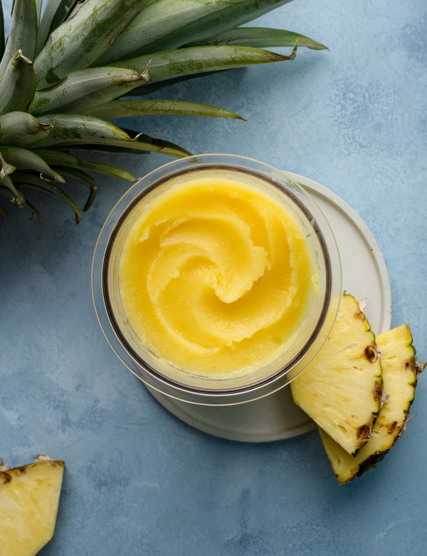Ninja creami pineapple sorbet in pint container on plate garnished with two pineapple chunks.