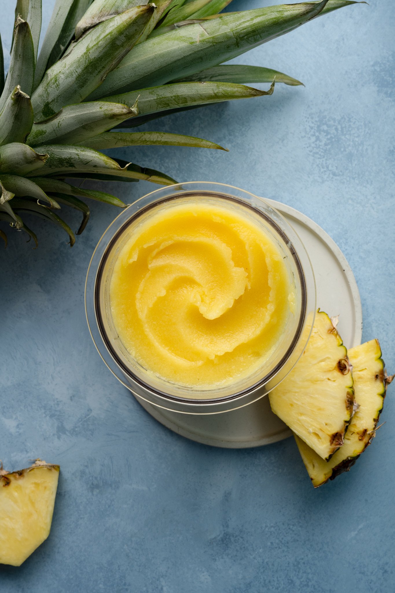 Ninja creami pineapple sorbet in pint container on plate garnished with two pineapple chunks.