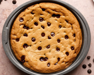 Close-up of the baked chocolate chip cookie cake still in the round metal baking pan, golden brown and studded with melted chocolate chips.