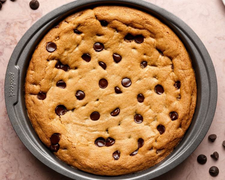 Close-up of the baked chocolate chip cookie cake still in the round metal baking pan, golden brown and studded with melted chocolate chips.