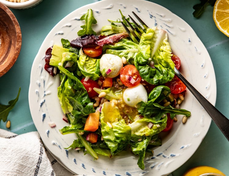 Plate of everyday salad on small white plate with fork and extra dressing drizzled on top.