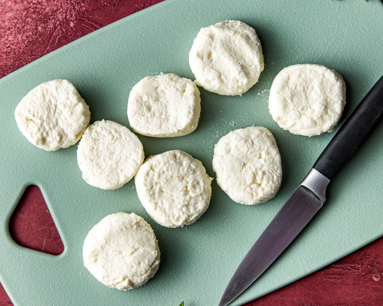 Frozen goat cheese medallions cut into 8 servings on green cutting board with knife.