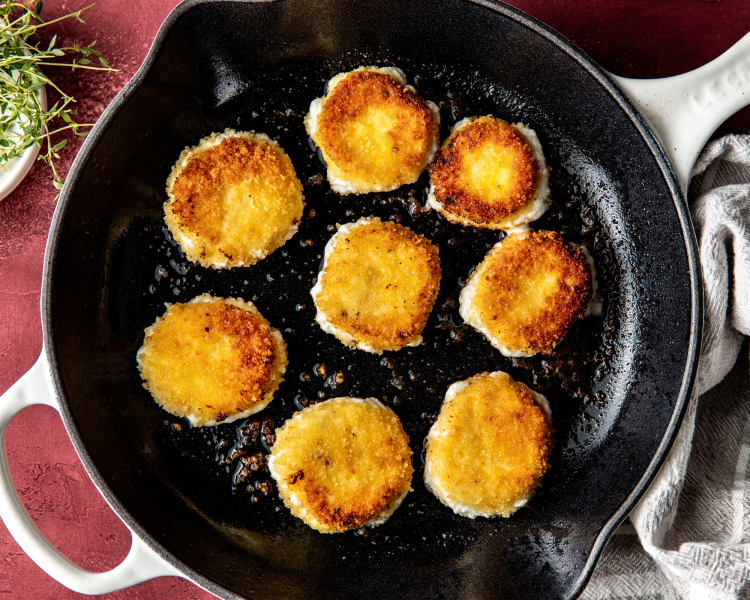 Eight goat cheese medallions frying in pan with oil.