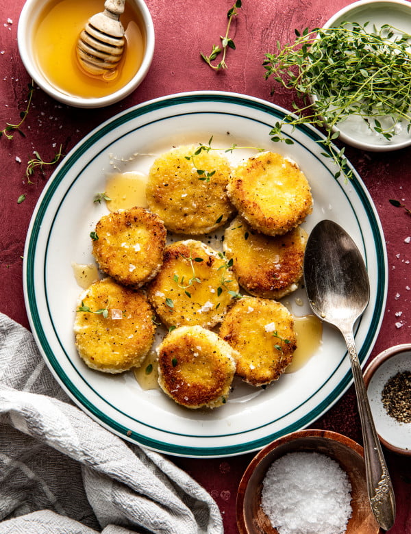 Fried goat cheese croutons on plate drizzled with honey and spoon on plate.
