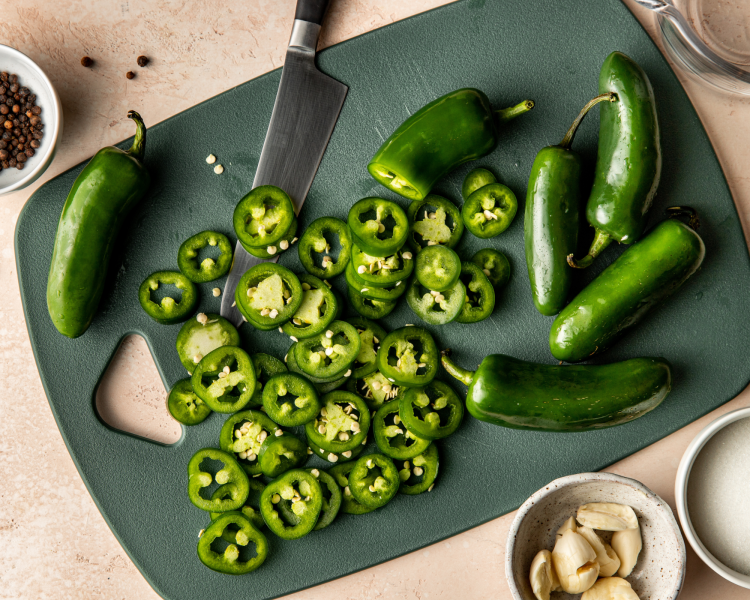 Chopping jalapenos on green cutting board.